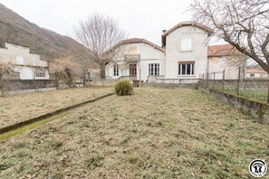 Ein zweistöckiges Haus mit kleinem Vorgarten, einer Holzterrasse und einer Steinmauer.