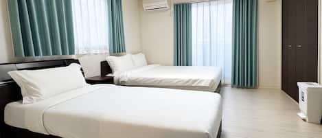 A hotel room with two beds, a wardrobe, an air conditioning unit, and a trash bin.