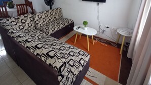A living room with a sofa, a small table, a fan, and a TV mounted on the wall. - Quiet house in gated community with A/C and Pool (Paseo de las Palmas II)