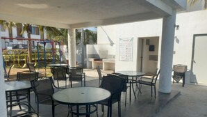 An outdoor patio area with round tables and chairs, a children's play structure, and a wall with a posted menu. - Quiet house in gated community with A/C and Pool (Paseo de las Palmas II)