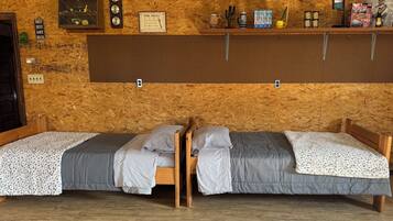 Een kamer met twee houten bedden, een prikbordwand en diverse spullen die op planken staan.