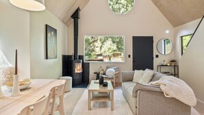 A cozy living room with a fireplace, a dining area, and a large window offering a view of greenery.