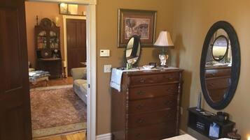A bedroom with a wooden dresser, a mirror, and a bed. There is a door leading to another room and a lamp on the dresser.