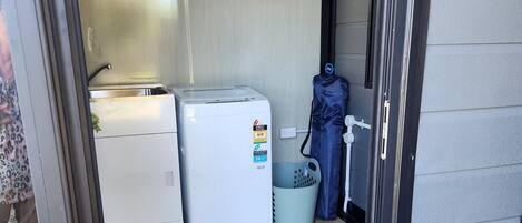 A compact kitchen with a washing machine, a small sink, and a trash bin.