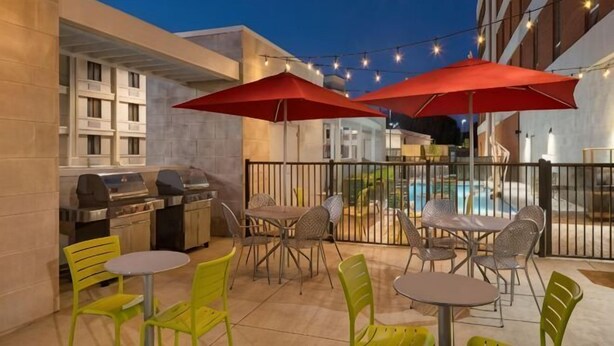 Un patio al aire libre con piscina, sombrillas rojas y mobiliario exterior.