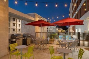An outdoor patio with a pool, red umbrellas, and outdoor seating. - Home2 Suites by Hilton Charlotte Airport (Charlotte)