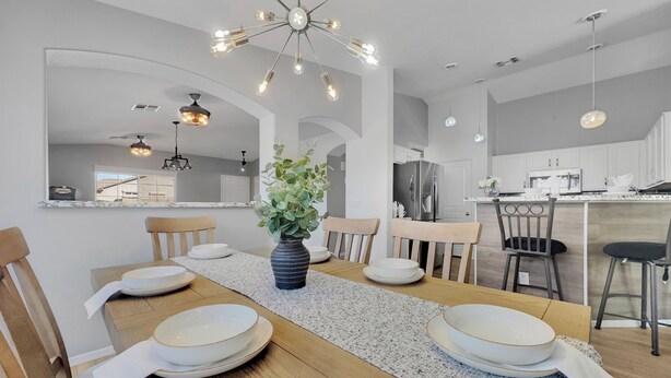 A modern kitchen with white cabinets, a central island, and a dining area with a wooden table and chairs. - Single-Level 4BR Surprise Home | Heated Pool, Game Room, Arcade (Surprise)