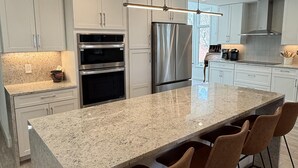 Uma cozinha moderna com armários brancos, eletrodomésticos de aço inoxidável, bancada de granito e banquetas.