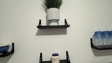 Un mur orné de trois étagères noires, chacune contenant des objets différents : une plante en pot, une tasse et un ensemble de verres.