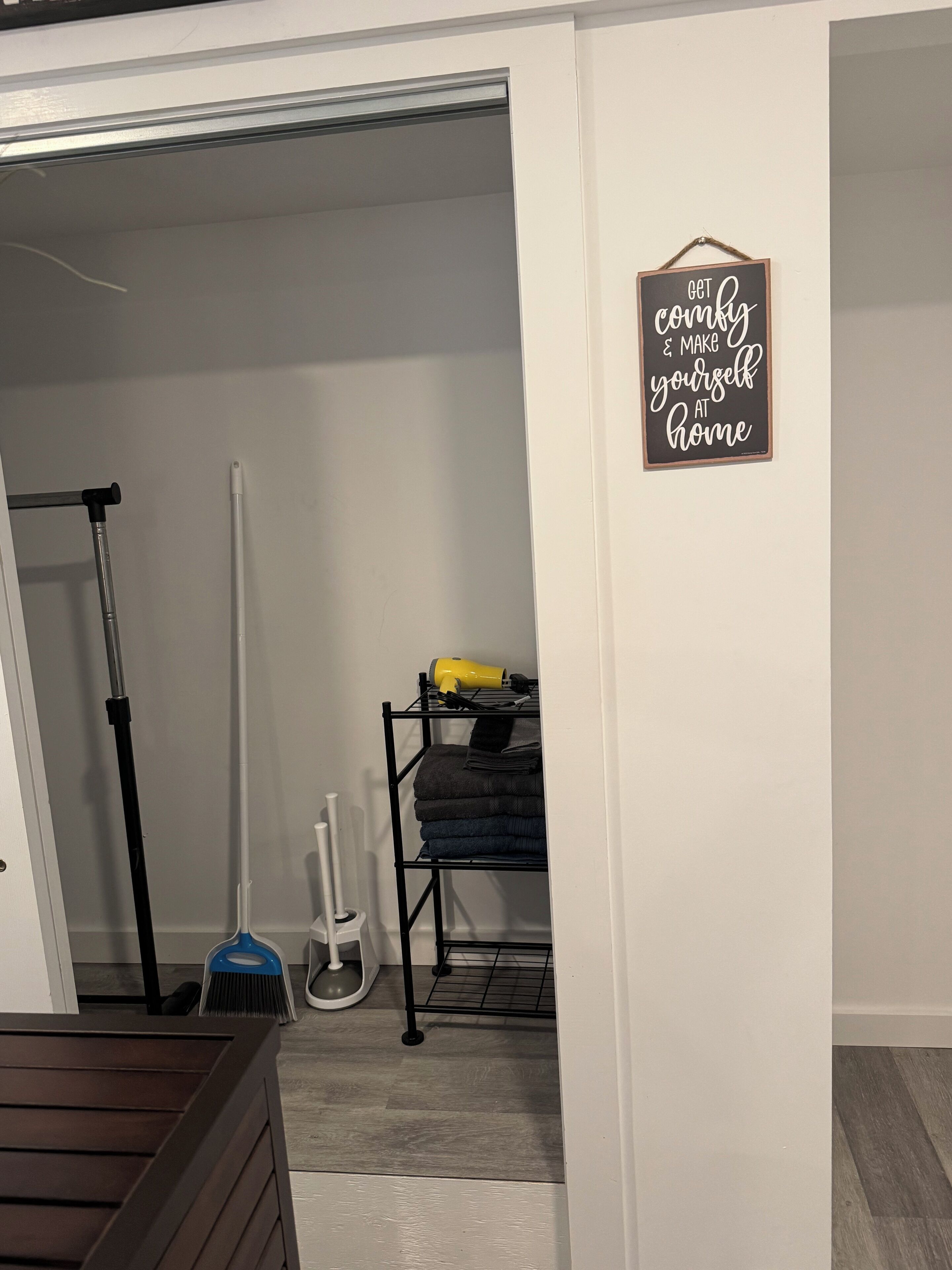 Een kamer met een witte muur, een bezem, een dweil en een plank met opgevouwen handdoeken.