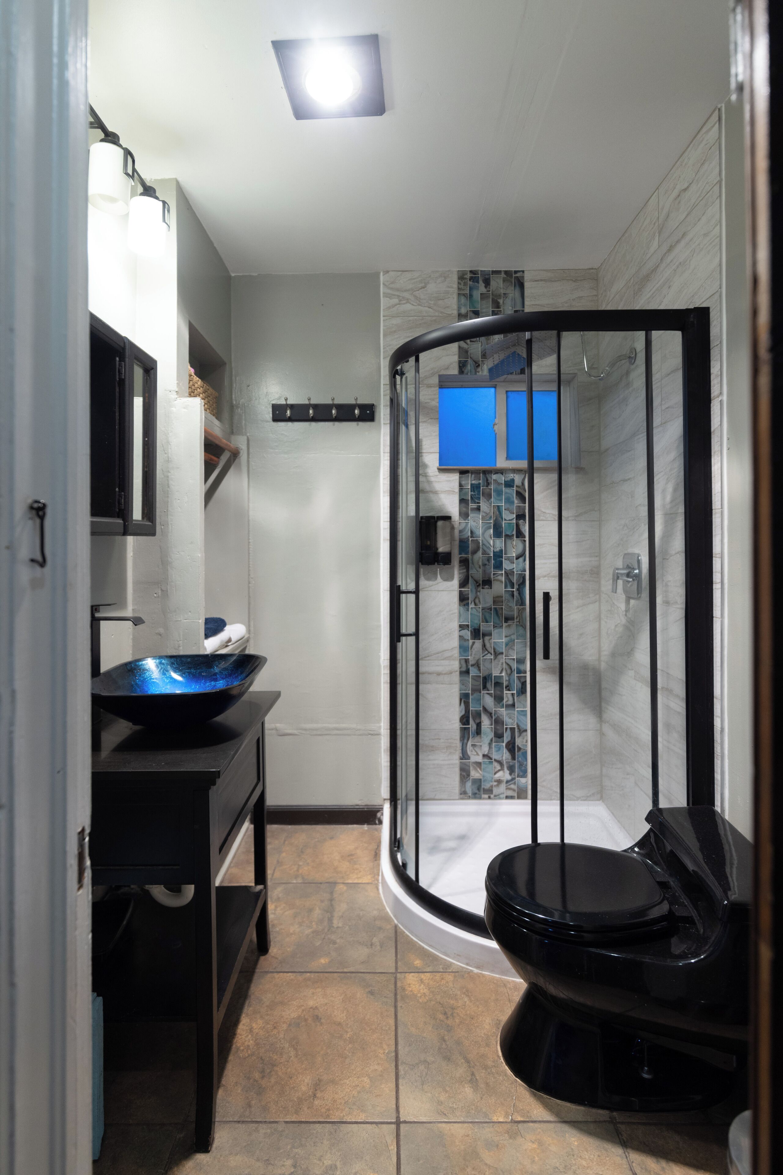 A compact bathroom with a glass shower enclosure, a black toilet, and a sink with a blue bowl.
