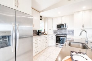 A modern kitchen with stainless steel appliances, white cabinetry, and a tiled backsplash. - Updated Canal Home with Dock for 25' Boat, Sandbar Access & Backcountry Fishing (Big Pine Key)
