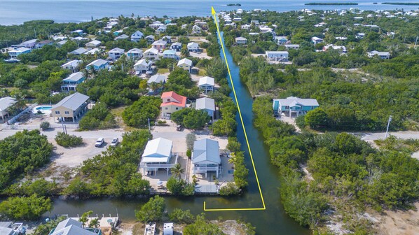 An aerial view of a coastal residential area with houses, a narrow waterway, and a dock.
