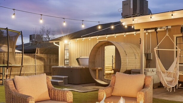 Un patio al aire libre con muebles de mimbre, un hogar para fuego y luces colgantes.