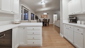 Una cocina moderna con armarios blancos, una isla central y un comedor al fondo.