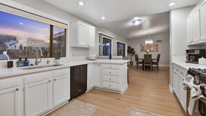 Una cocina moderna con armarios blancos, lavavajillas y un comedor con candelabro.