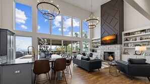 A spacious living area with a fireplace, large windows, and a modern kitchen. - Blue Ridge Mountain Retreat, Panoramic Views, Game Room, and Hot Tub! (Blue Ridge)