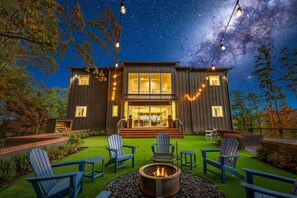 A modern house with a fire pit and outdoor seating, surrounded by a well-maintained lawn and trees. - Blue Ridge Mountain Retreat, Panoramic Views, Game Room, and Hot Tub! (Blue Ridge)