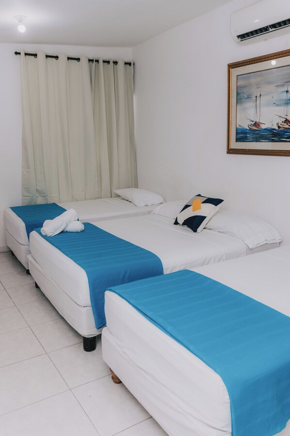 A hotel room with two single beds, a large window with curtains, a painting on the wall, and an air conditioning unit. - Hotel Ibatama (Cartagena)