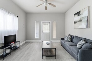 A modern living room with a grey sofa, a black coffee table, a TV on a black stand, and a ceiling fan. - Spacious 2BR Duplex Near Downtown San Antonio (San Antonio)