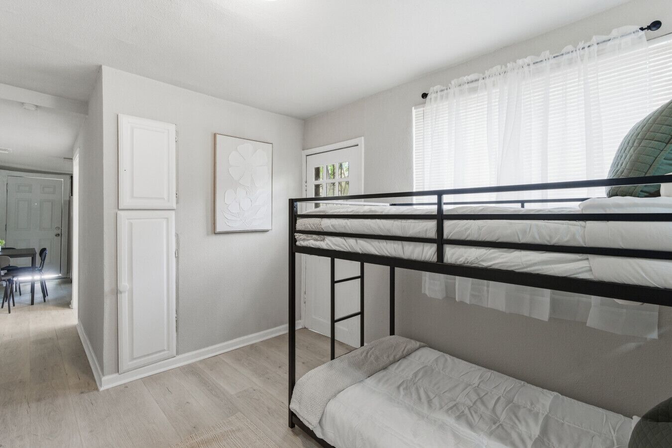 Dormitorio con literas, una puerta, un cuadro enmarcado y una ventana con cortinas.