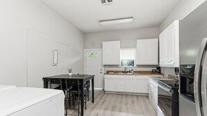 A compact kitchen with white cabinets, a black dining table, and a stainless steel refrigerator. - Bright 2BR Duplex Mins to Downtown San Antonio (San Antonio)
