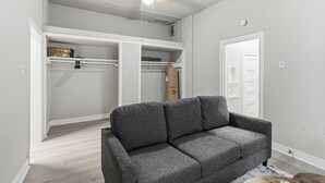 A room with a grey sofa, a ceiling fan, a closet with white shelving, and a door with a decorative panel. - Bright 2BR Duplex Mins to Downtown San Antonio (San Antonio)