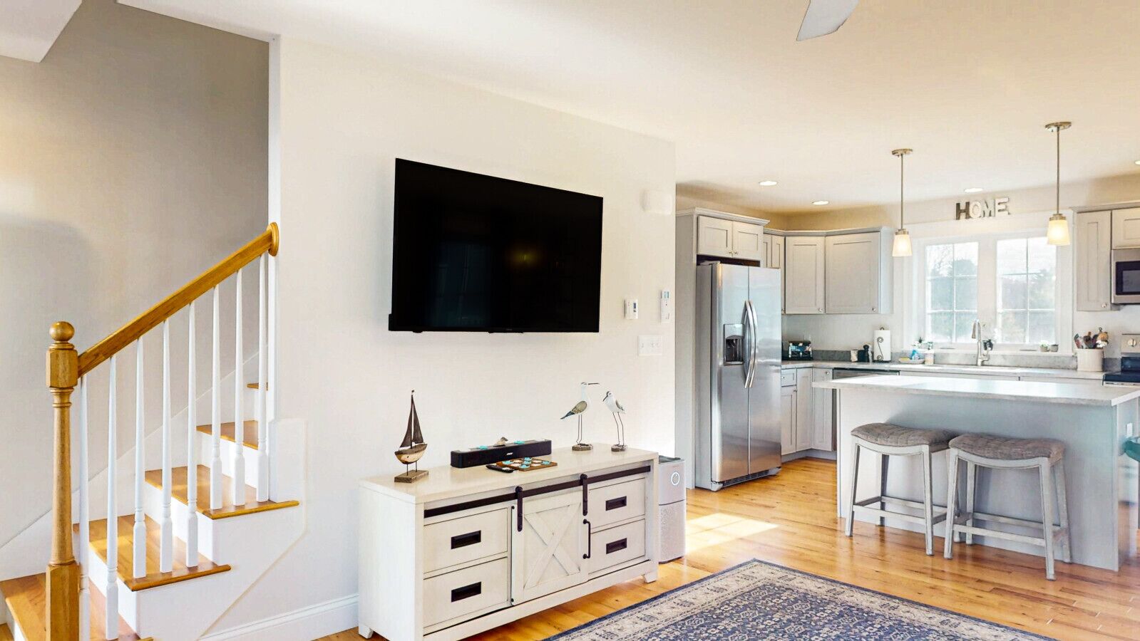 A modern kitchen with a central island, white cabinetry, a stainless steel refrigerator, and a flat-screen TV mounted above the island.