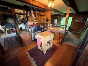 Une cuisine rustique avec des poutres en bois, un poêle et une table à manger surmontée d’un tapis.