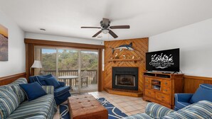 Een woonkamer met een open haard, een plafondventilator en een televisie waarop 'Coastal Carolina Vacations and Sales' staat.