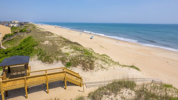 Een strand met een houten pier die uitkomt bij een gazebo, met uitzicht op de oceaan.