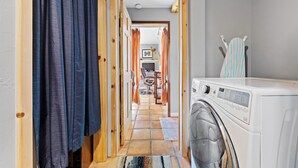 Un lavadero con lavadora, una puerta de madera y suelo de baldosas que conduce a una sala de estar.