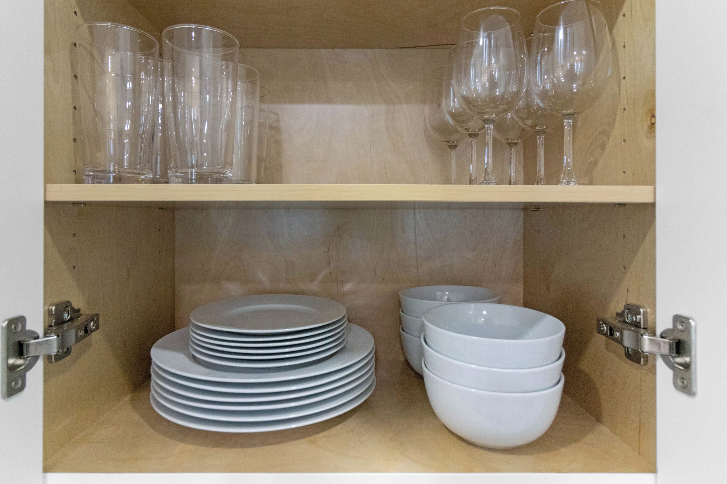 A wooden cabinet with shelves holding clear glasses and stacked white plates and bowls.