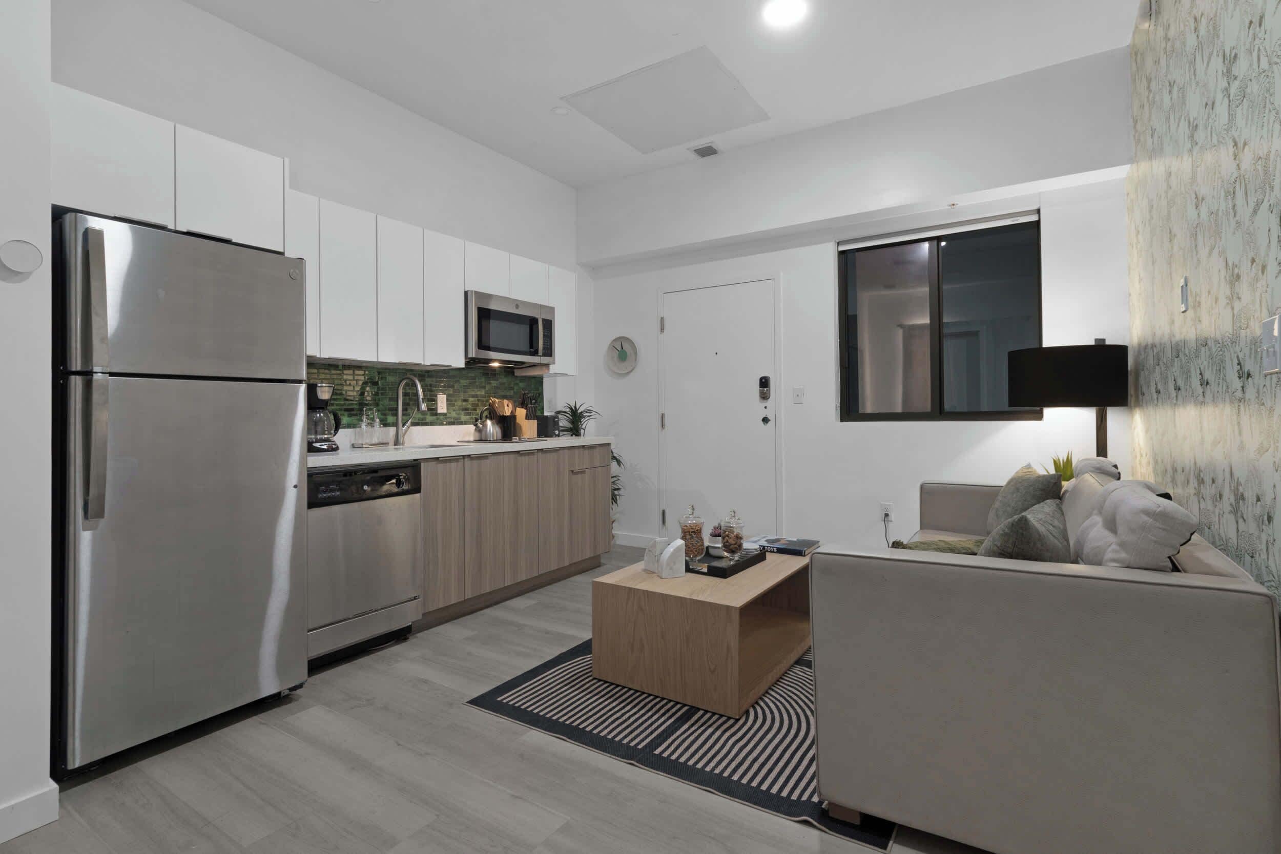 A modern kitchen with stainless steel appliances, a microwave, and a dishwasher. There is a wooden coffee table and a sofa with cushions.