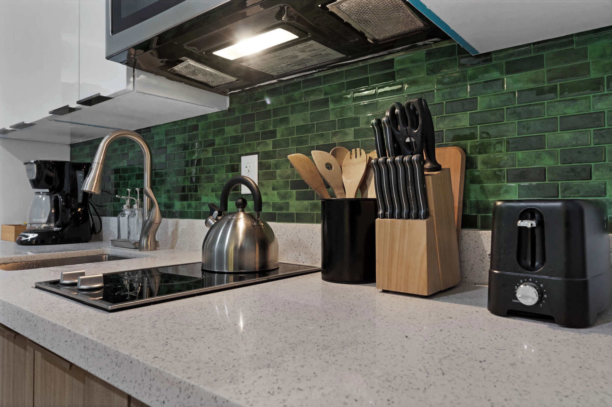 Eine moderne Küche mit einem grün gefliesten Rückwand, einem Wasserkocher, einer Kaffeemaschine, einem Toaster und einem Messerblock.