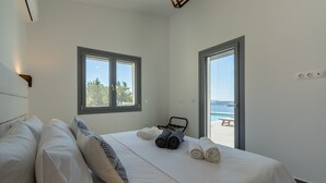 A bedroom with a large bed, two windows, and a view of the beach.