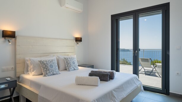 A bedroom with a large bed, two bedside tables, a nightstand, a sliding glass door leading to an outdoor area with a chair and table.