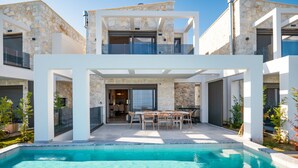 A modern two-story house with a swimming pool, outdoor dining area, and stone facade.