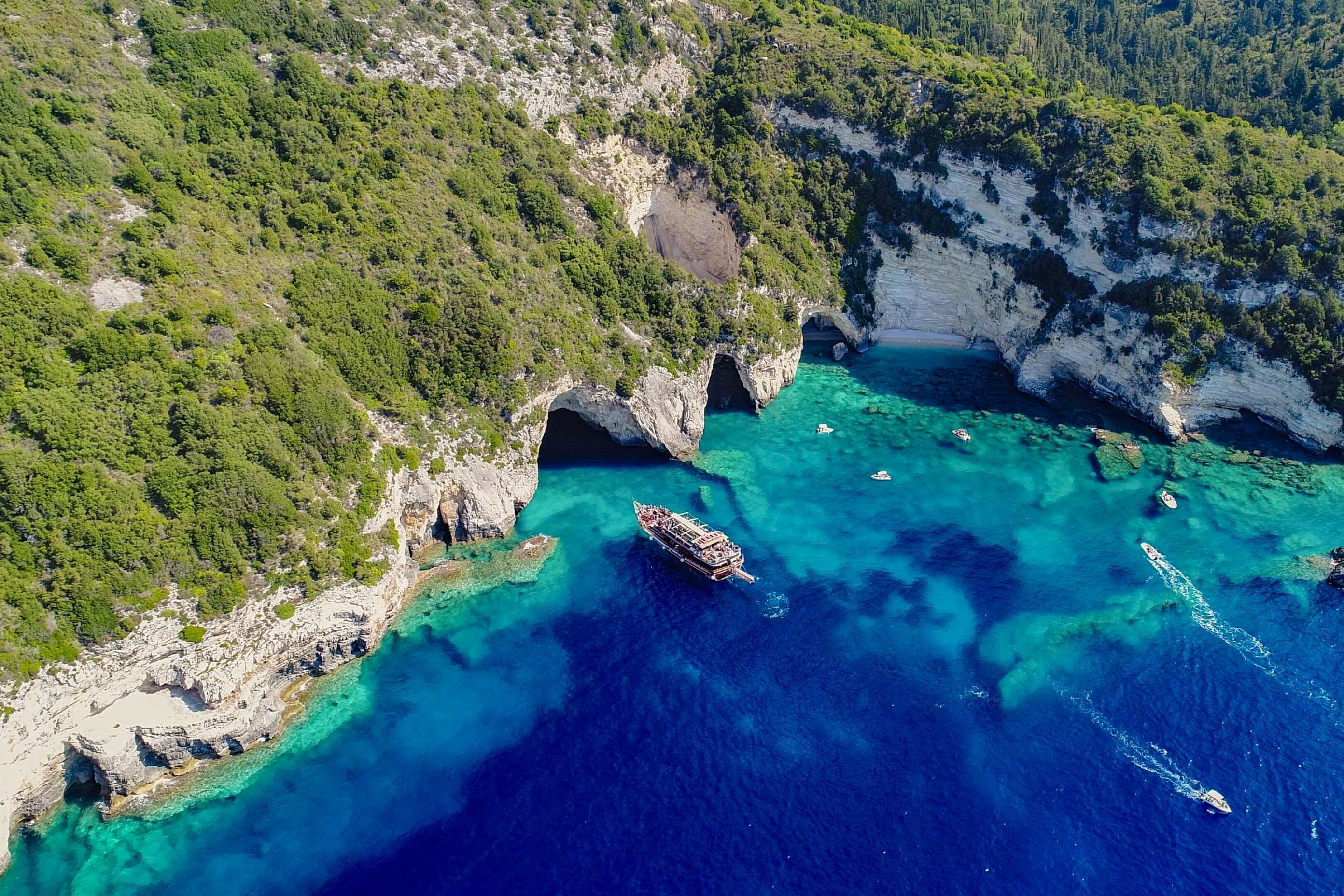 Vue aérienne d’une zone côtière avec des falaises, des eaux turquoise et limpides, et des bateaux.