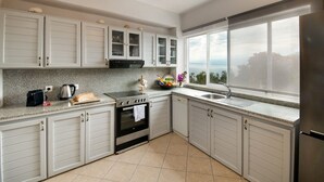 A modern kitchen with white cabinets, a granite countertop, a built-in oven, and a large window offering a view. - Thodoros Apartment – 3 Bedrooms, Sea Views, Family-Friendly (Boikatika Erimitis)