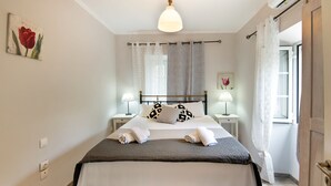A neatly made bed with a grey and white duvet, two bedside lamps, and a wall-mounted artwork of a red tulip. - Thodoros Apartment – 3 Bedrooms, Sea Views, Family-Friendly (Boikatika Erimitis)