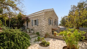 A stone house with a tiled roof, a small porch, and potted plants. - Thodoros Apartment – 3 Bedrooms, Sea Views, Family-Friendly (Boikatika Erimitis)