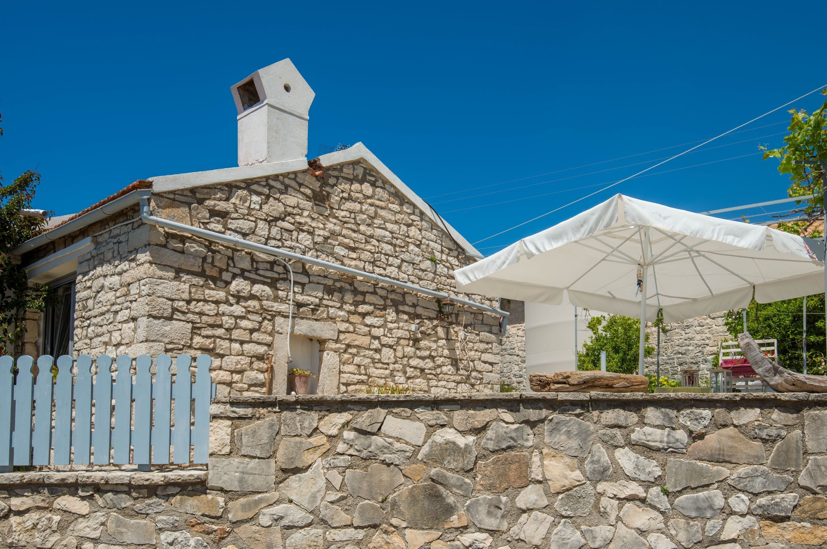 A stone building with a chimney, a white fence, and a white umbrella.