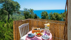 Una mesa con platos, cubiertos, una botella y una copa, con vistas a un paisaje marino y arbolado.