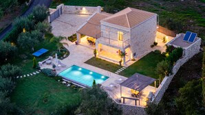 Ein zweistöckiges Steinhaus mit Swimmingpool, Sitzgelegenheiten im Freien und Solaranlage.