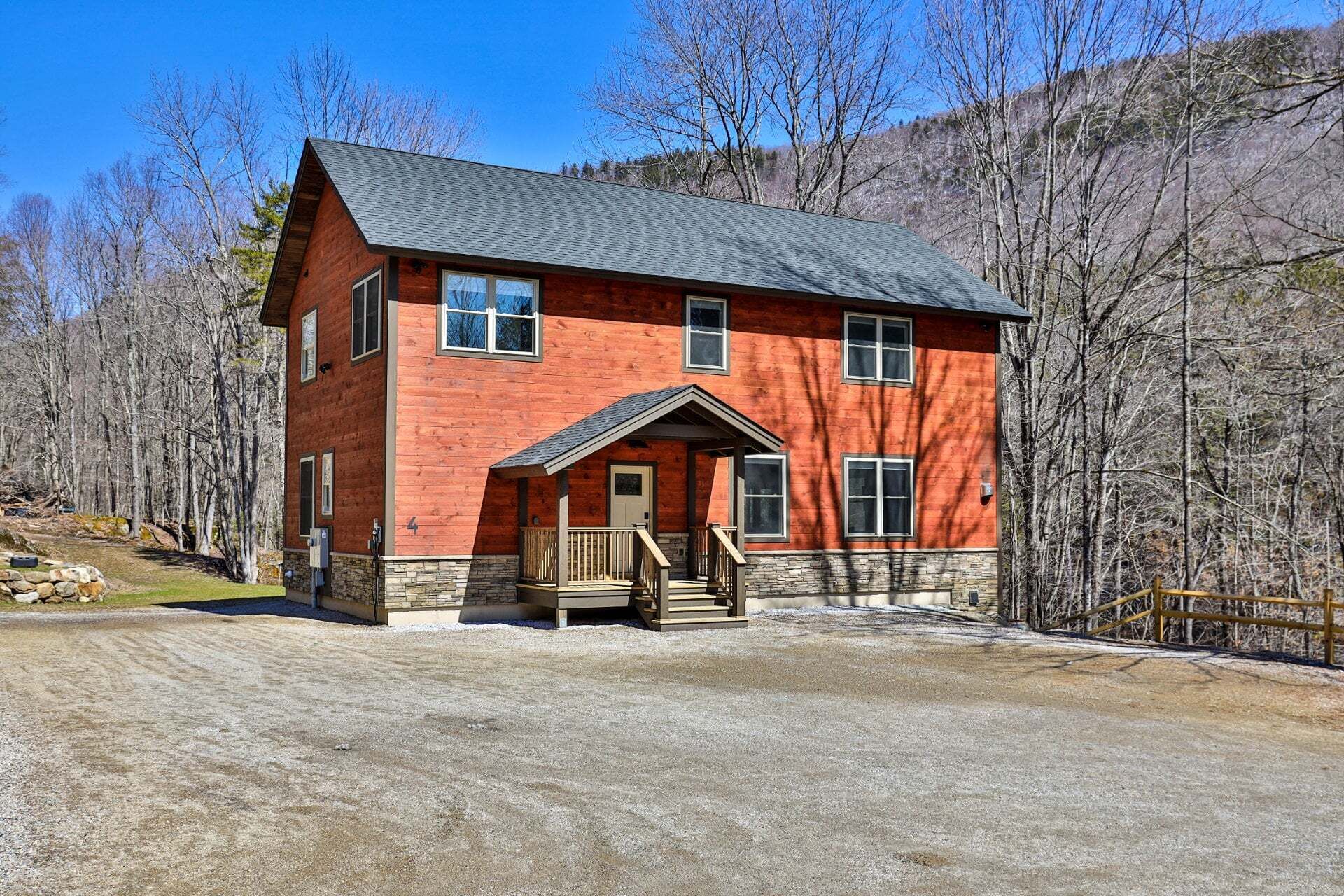 A two-story log cabin with a stone foundation, a porch, and a gravel driveway.