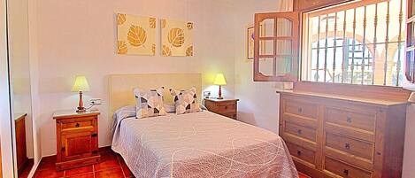A bedroom with a bed, two nightstands with lamps, a dresser, and a window with bars.