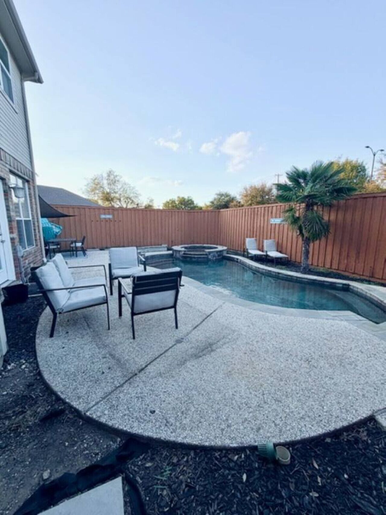 Un jardin avec une piscine, une clôture en bois et du mobilier d’extérieur.