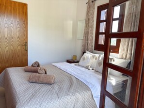 Ein Schlafzimmer mit einer Holztür, einem Bett mit weißer Bettwäsche, einem Nachttisch und einem Spiegel.