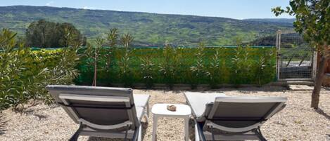 Two lounge chairs facing a table with a view of a hilly landscape.